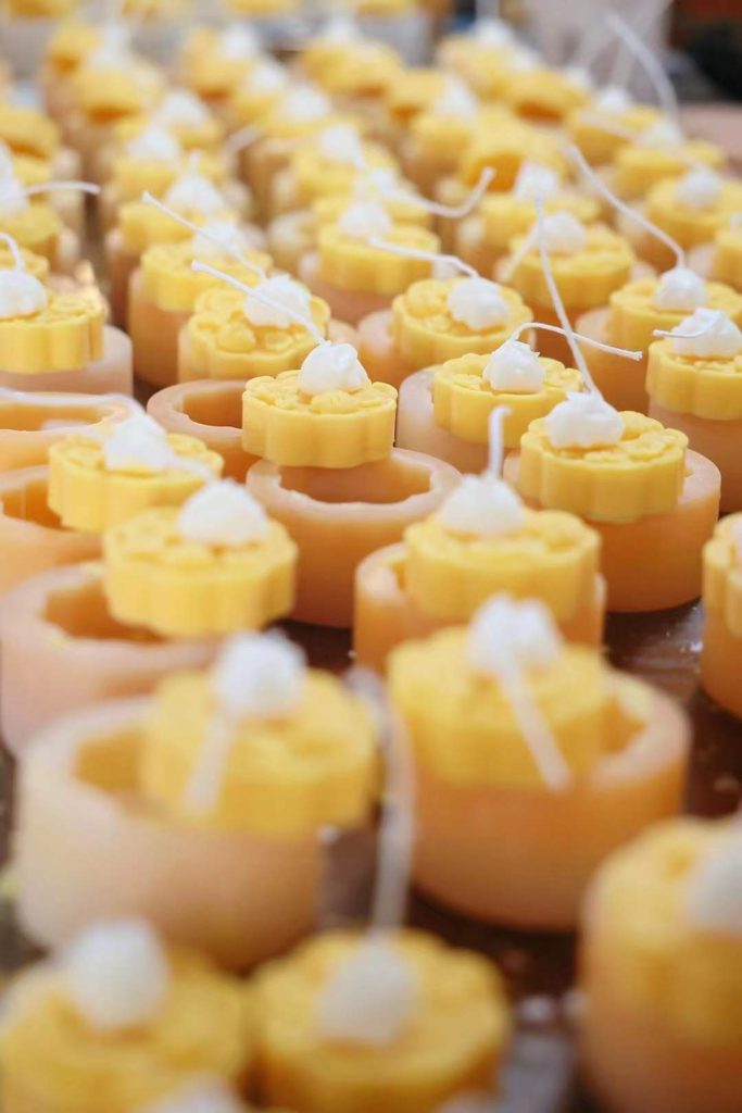 Factory assembly line crafting custom yellow dessert cup soy candles with handcrafted wax whipped cream embeds and cotton wicks.