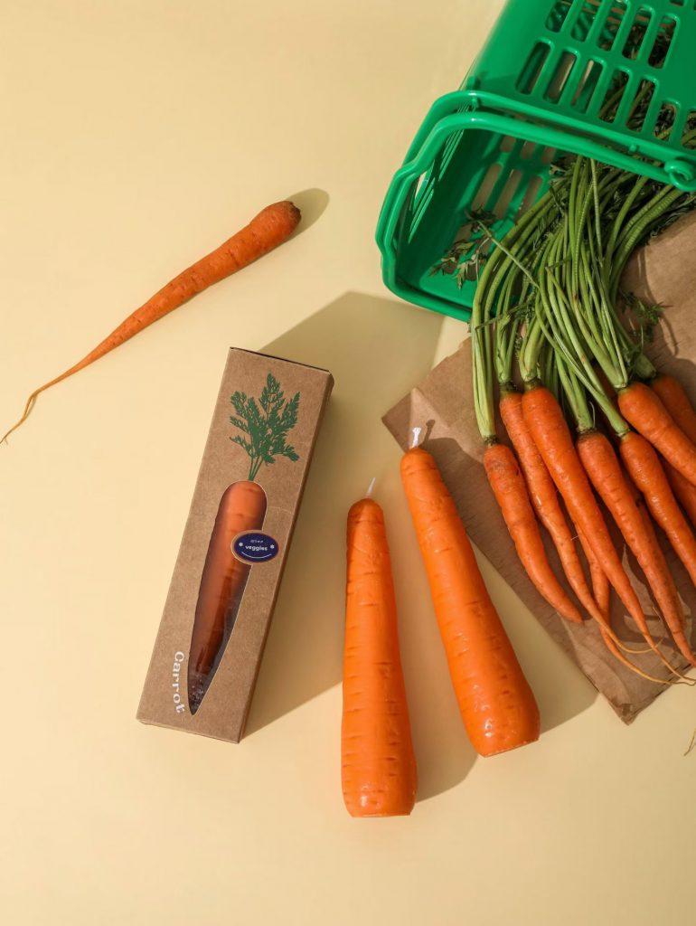 Realistic orange carrot shaped soy candles with green tops in shopping basket