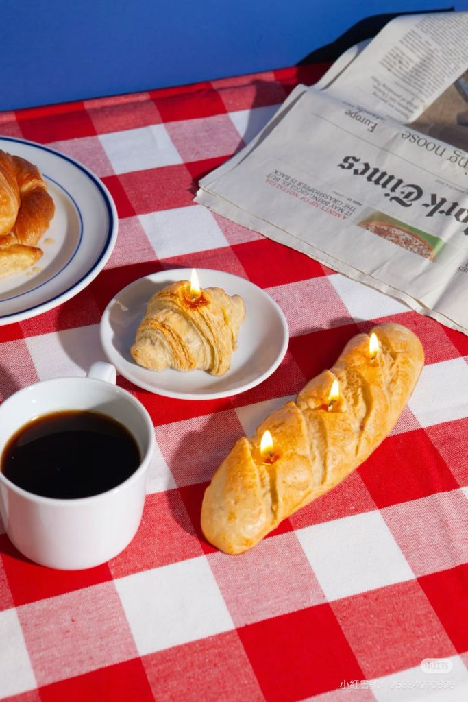 Hyper-realistic multi-wick French baguette and croissant pastry scented soy candles styled with coffee for bakery home decor wholesale sourcing.