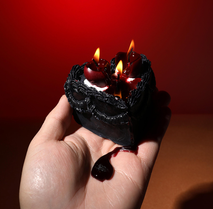 Burning black gothic heart dessert candle showing dramatic blood red bleeding wax melt drip effect for Halloween and luxury gifting