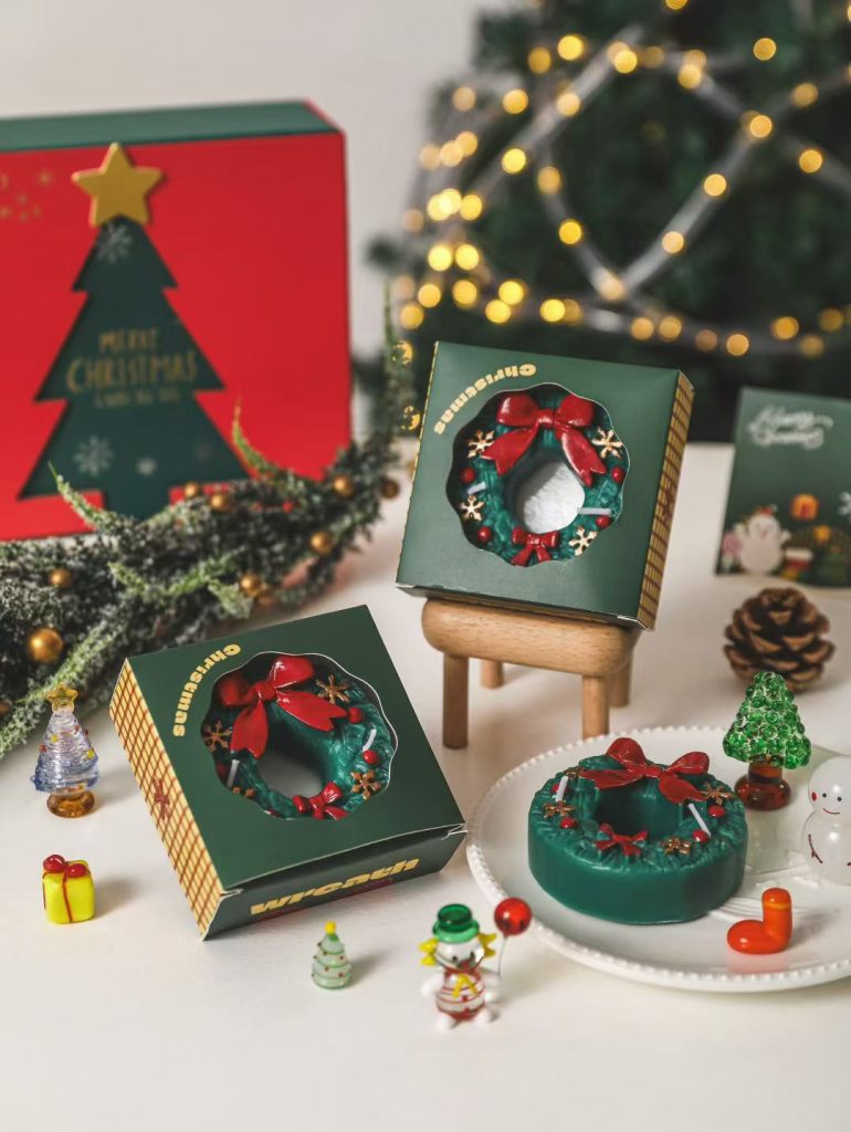 Decorative green Christmas wreath soy candle with red bow accent and bespoke holiday packaging box.