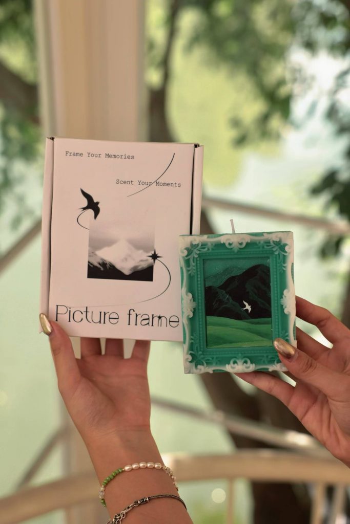 Hands holding custom green oil painting picture frame candle and presentation gift box