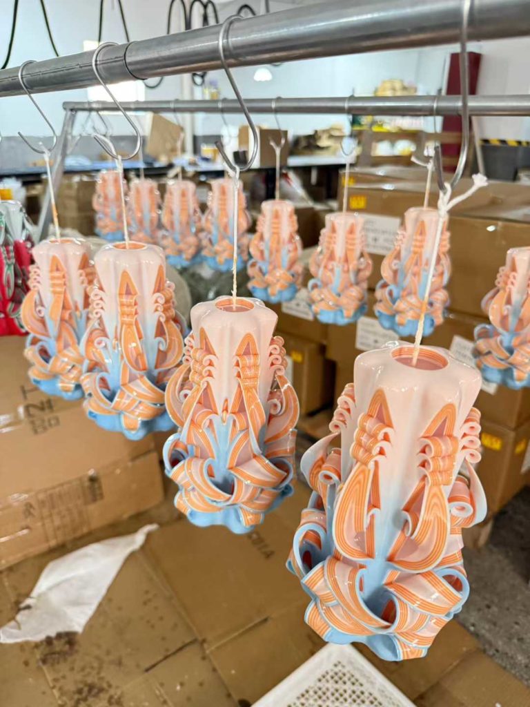Artisanal multi layer wax dipped candles hanging on factory drying racks during the hand carving process