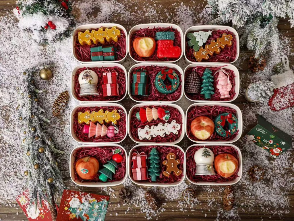 Assorted novelty Christmas candle gift sets in printed metal bento tin boxes including mini trees, wreaths, and gingerbread men.